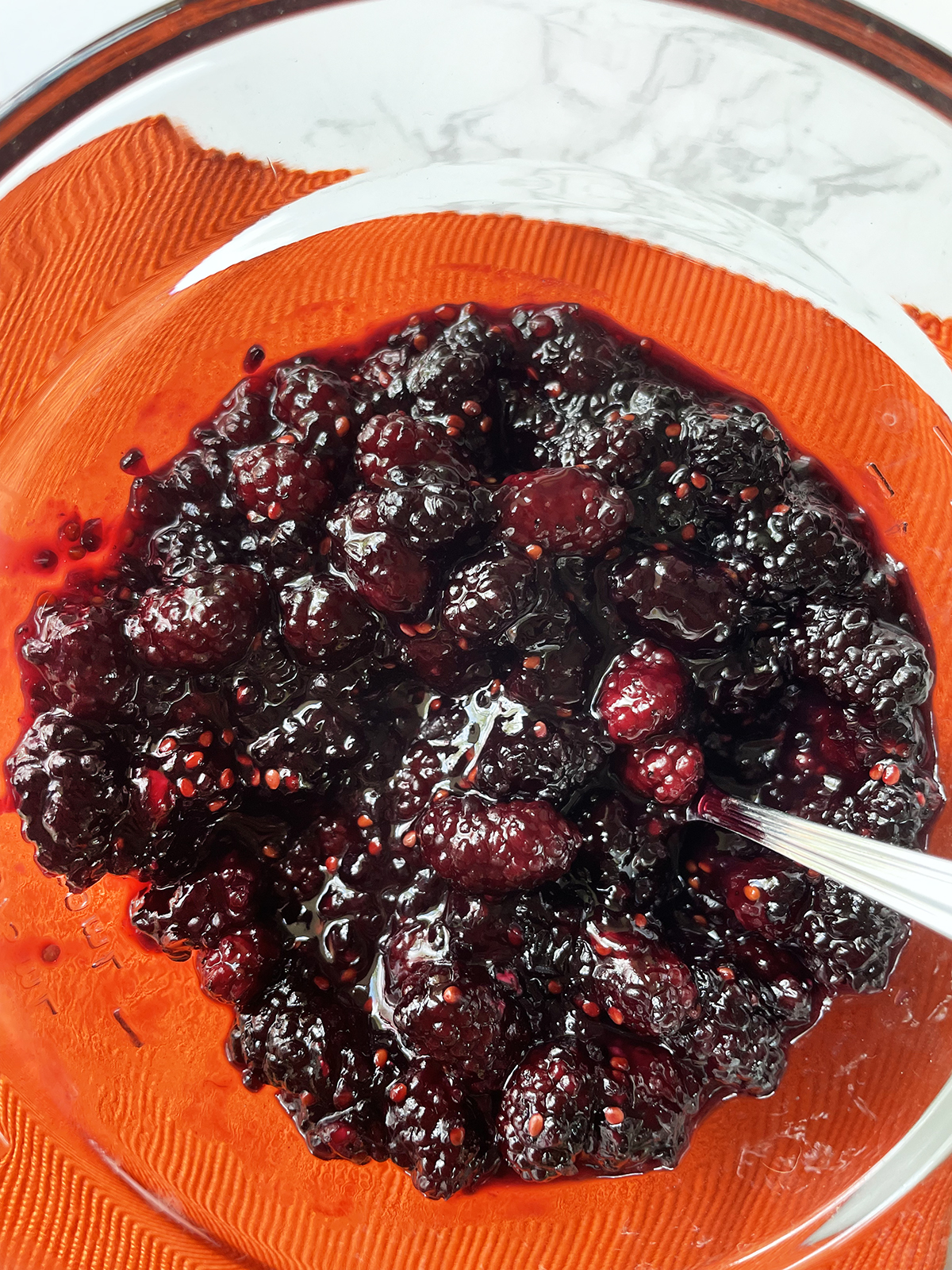 Mulberry sauce in a glass bowl with a spoon inside.