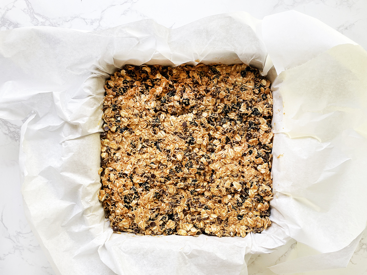 Granola bar mixture in a baking dish with parchment paper.