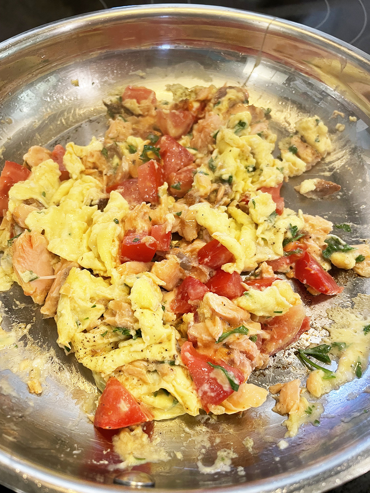 Egg scramble with salmon and tomatoes in a skillet.