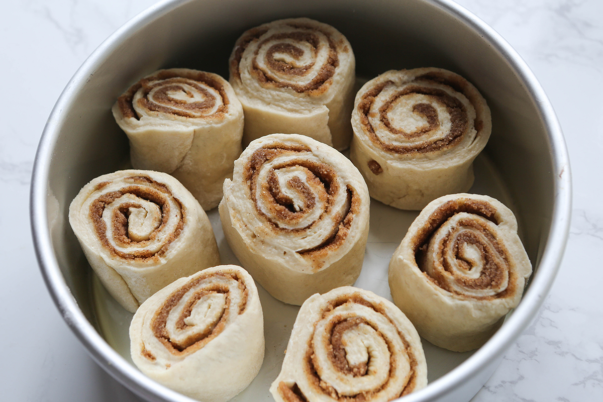 Eight cinnamon roll pieces arranged in a round cake pan.