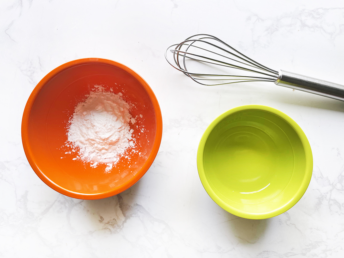 Corn starch and water in separate small bowls with a whisk next to them.