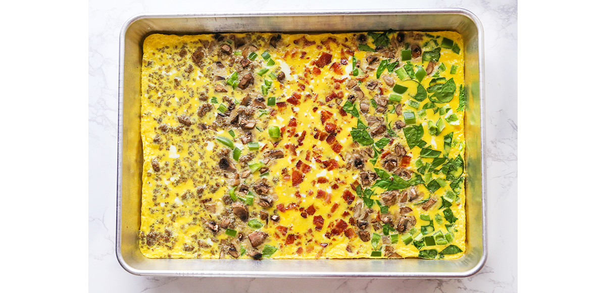 Pan of cooked eggs with other breakfast meats and toppings layered in strips crosswise.