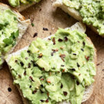 Top view of a few pieces of avocado toast on a cutting board with seasoning on top.