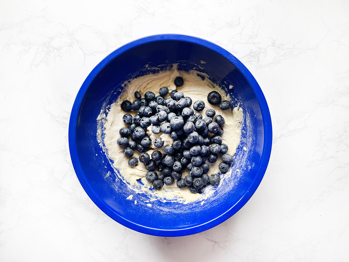 Mixing bowl filled with muffin batter and fresh blueberries on top.