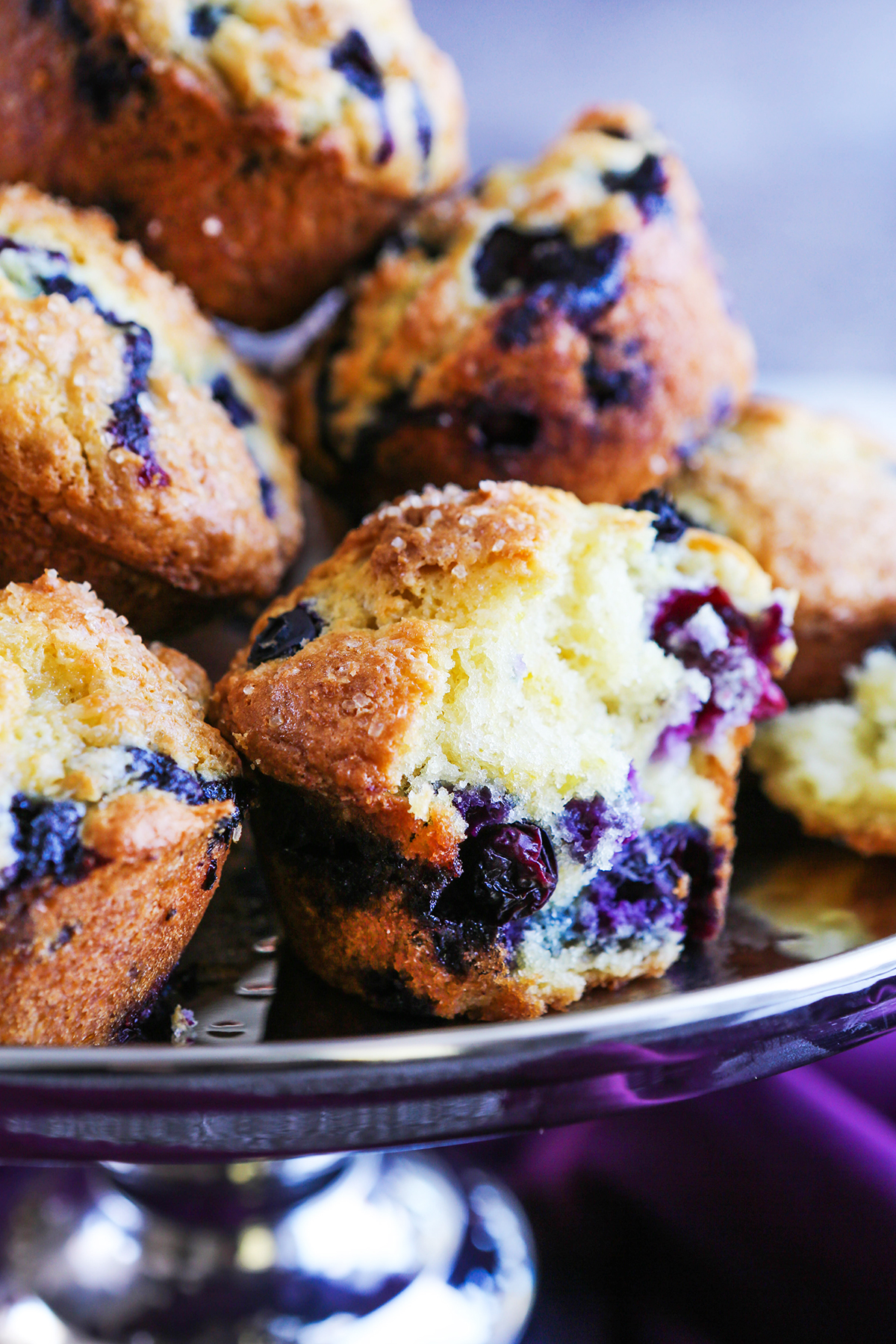 Tall stack of blueberry muffins on a footed cake plate.