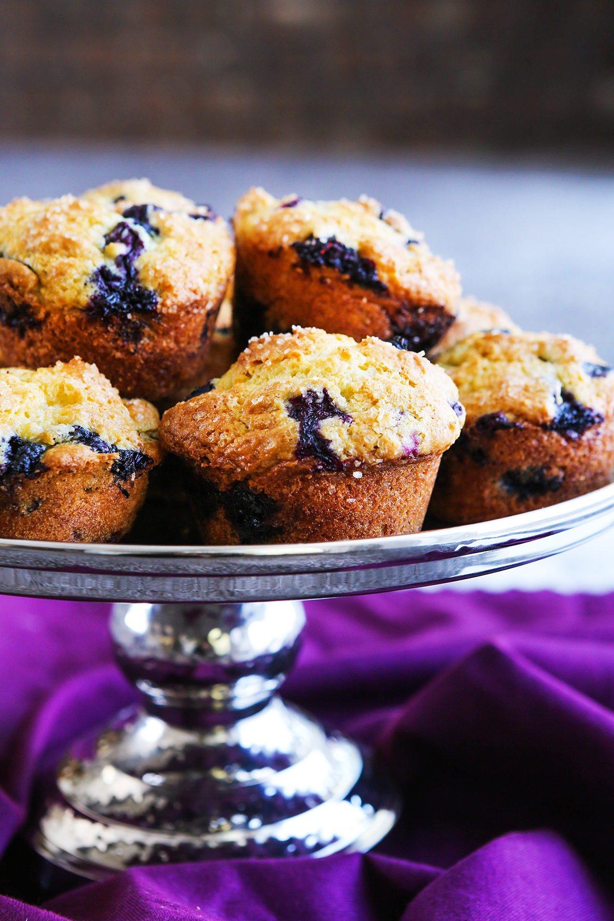 Blueberry muffins stacked on a silver cake plate, ready to eat.