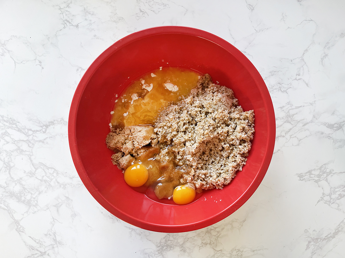 Cooked steel cut oats, eggs and other wet ingredients in a red bowl.