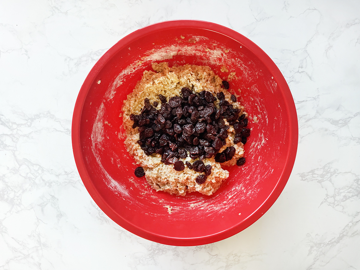 Wet ingredients with dried fruit on top, in a red mixing bowl.