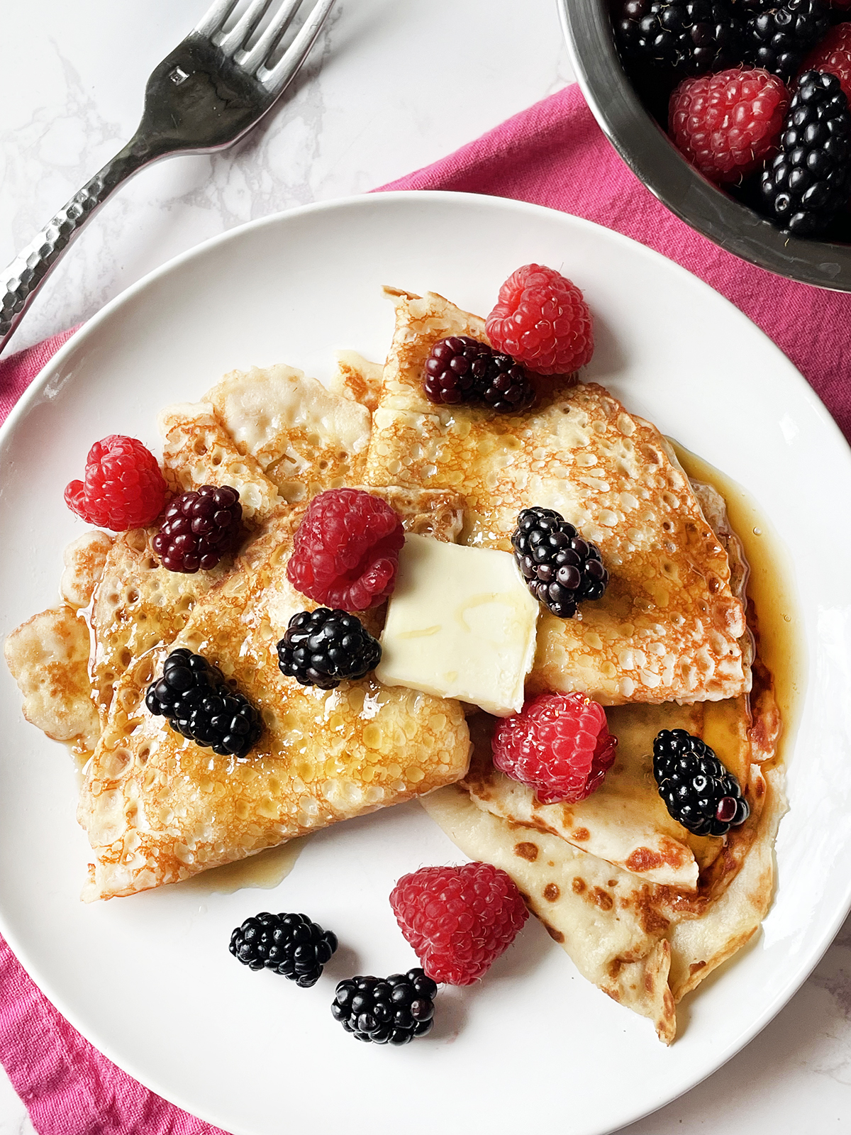 Top view of a plate of crepes topped with syrup and berries.