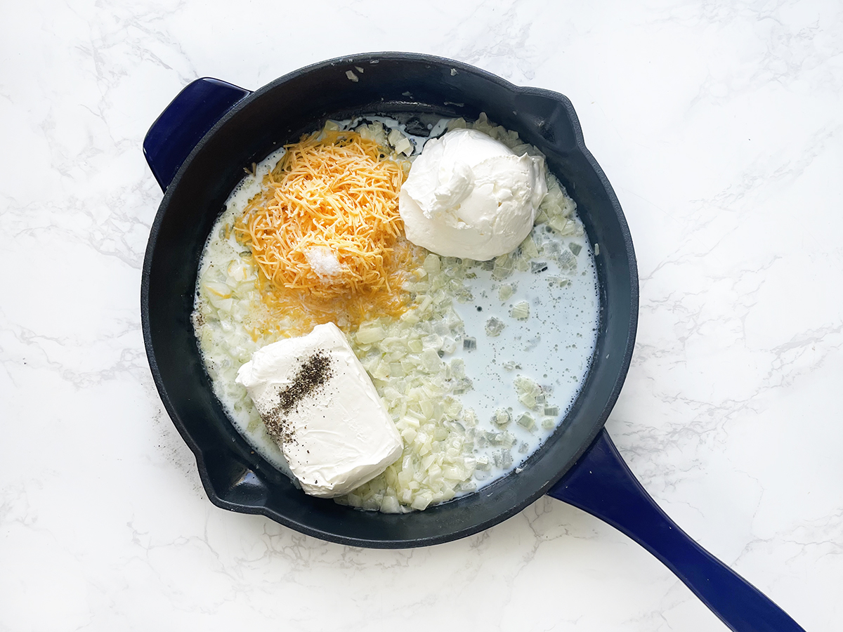Cheeses, onions and milk in a skillet, ready to cook.