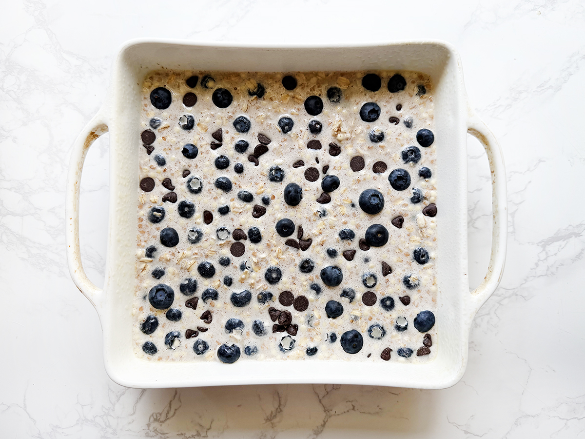 Oatmeal mixture in a square pan with blueberries, ready to bake.