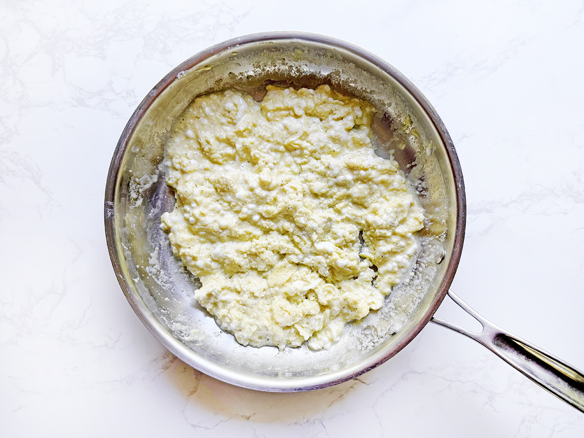 Cooked scrambled eggs and cottage cheese in a skillet.
