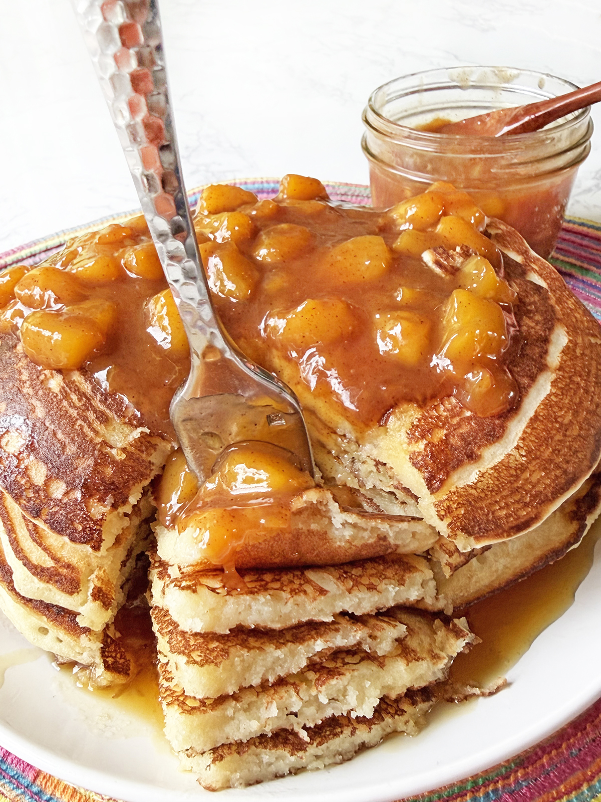 Fork digging into a stack of pancakes topped with a peach sauce.