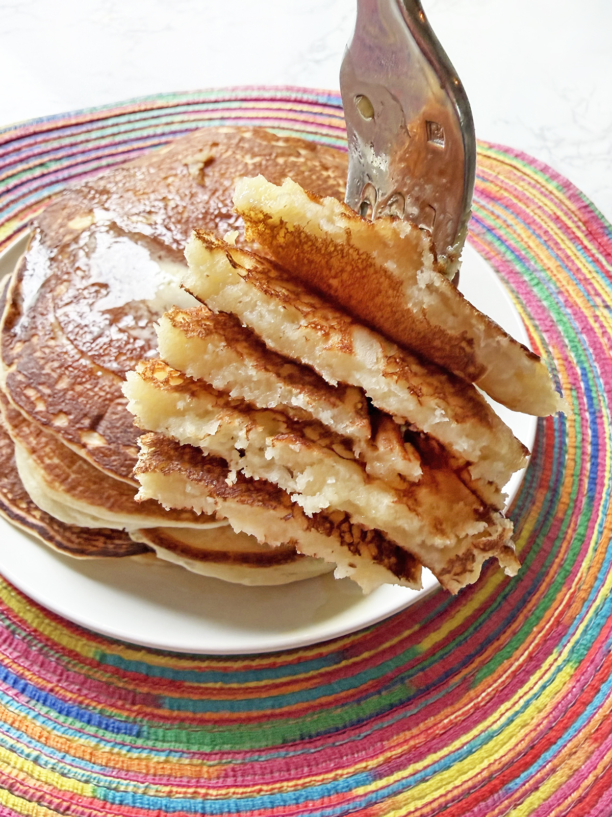Fork with a stacked bite of pancakes soaked with syrup.
