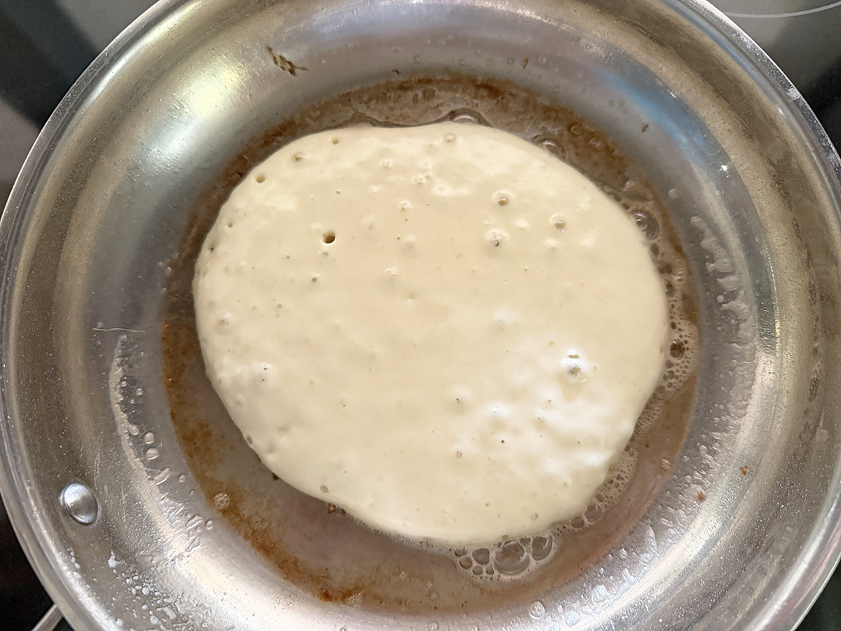 Pancake cooking in a skillet with bubbles on top.
