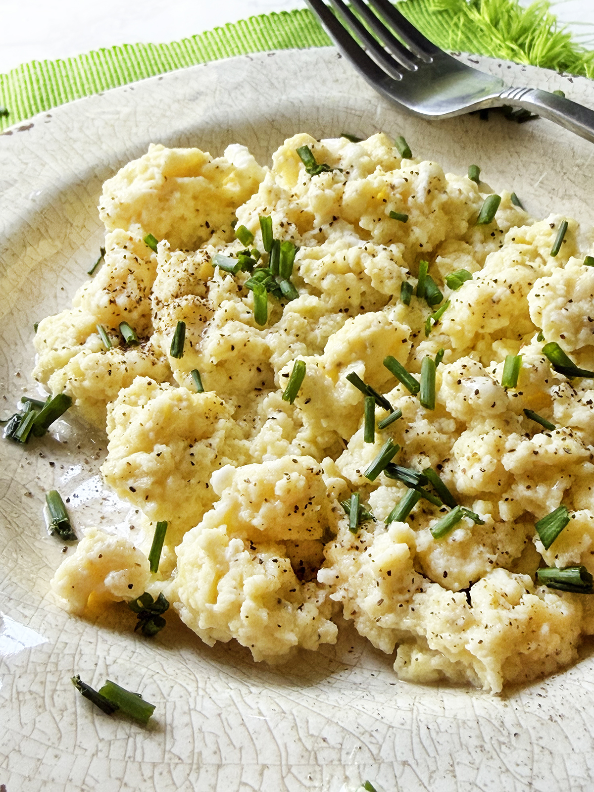 Closeup of a plate of fluffy scrambled eggs with cottage cheese and chives.