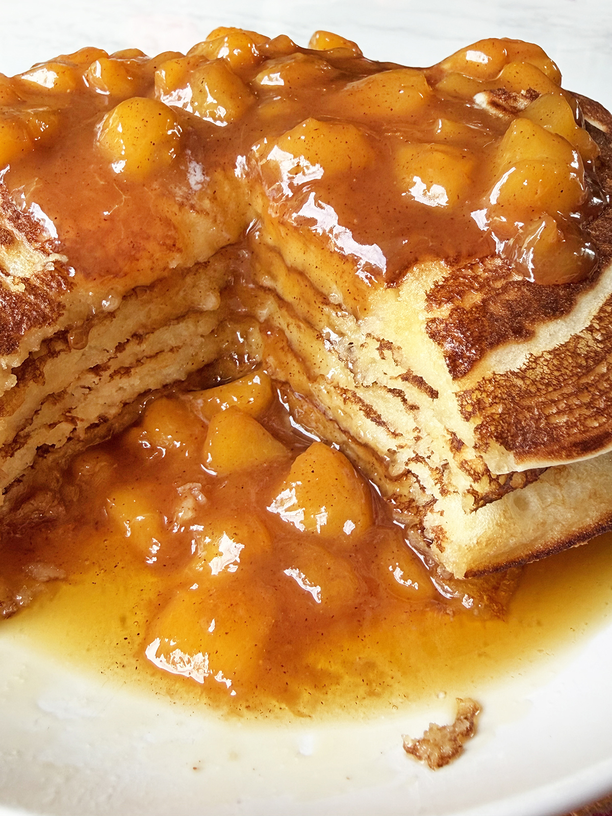 Stack of pancakes with peach sauce, with a giant bite removed.
