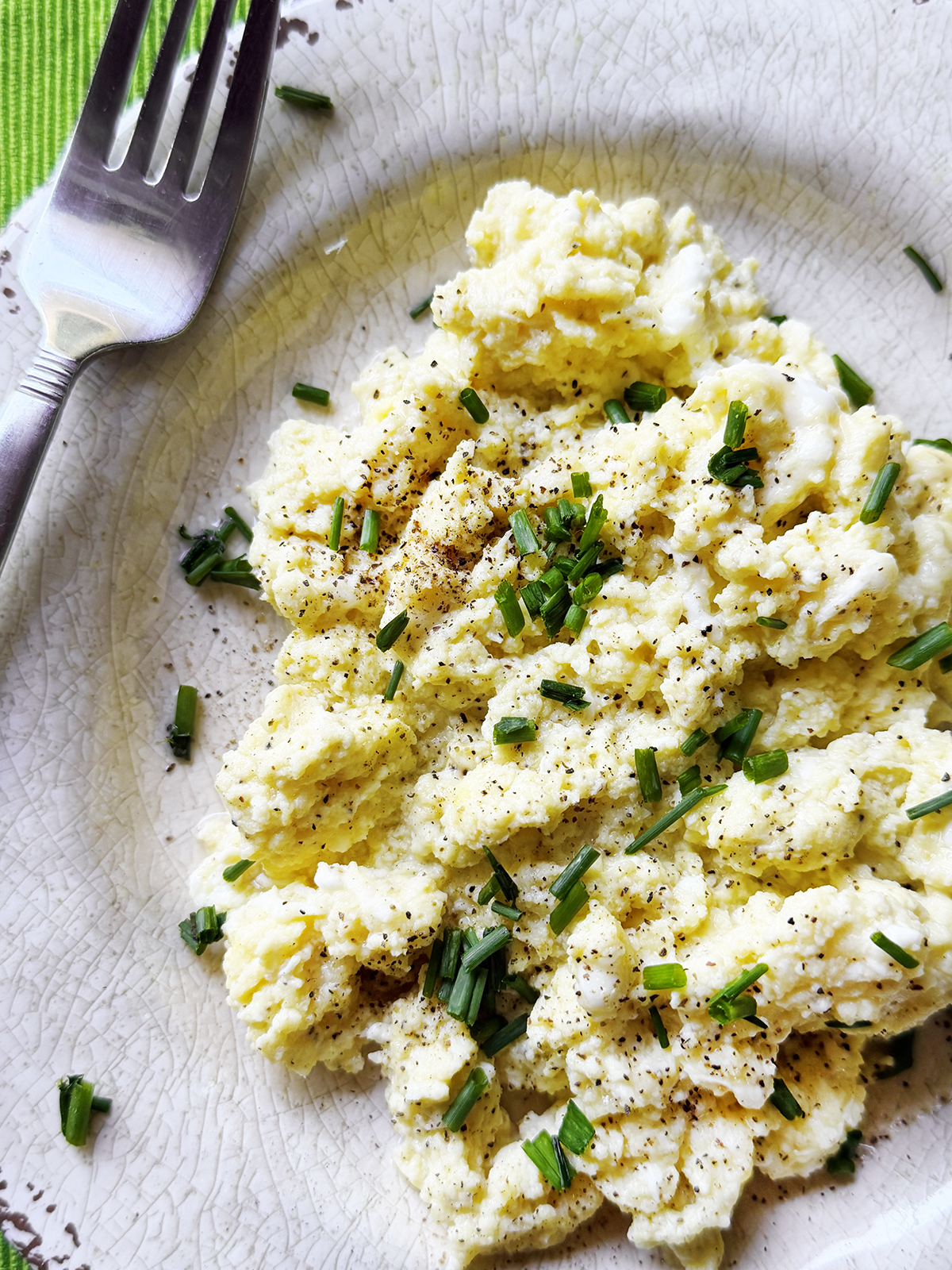 Top view of a plate of scrambled eggs with cottage cheese and chives on top.